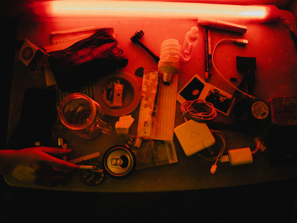 Una mesa con lata aplastada, cigarros, pipas, fotos instantaneas y una luz roja